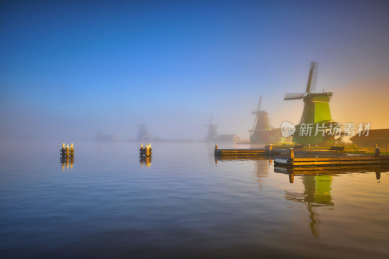 荷兰传统的风车在日出时的薄雾中沿着Zaanse Schans运河在荷兰。